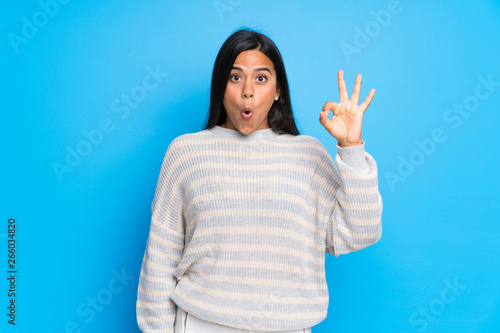 Young Colombian girl with sweater surprised and showing ok sign