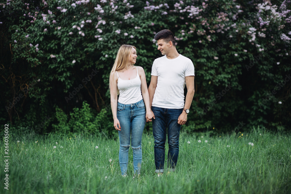 A young couple in love holding hands in front of a flowering bush A young couple in love holding hands in front of a flowering bush
