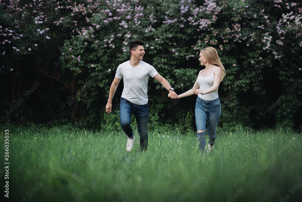 A young couple in love holding hands and running forward in front of a flowering bush