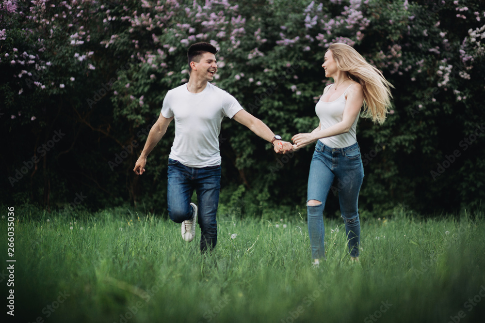 A young couple in love holding hands and running forward in front of a flowering bush A young couple in love holding hands and running forward in front of a flowering bush