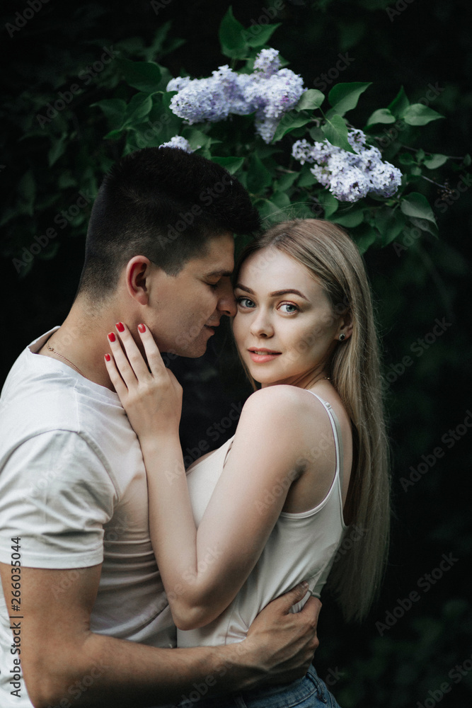 A romantic couple in love hugging in front of a flowering bush