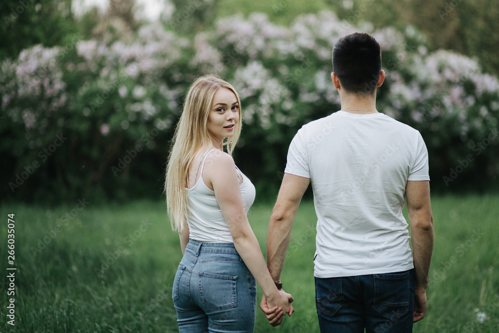 A young couple in love holding hands and walking towards the flowering bush A young couple in love holding hands and walking towards the flowering bush