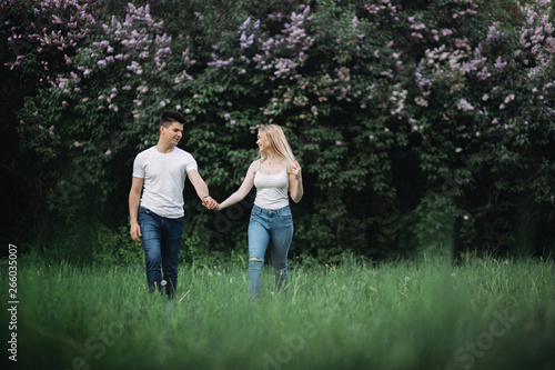 A young couple in love holding hands and walking forward in front of a flowering bush