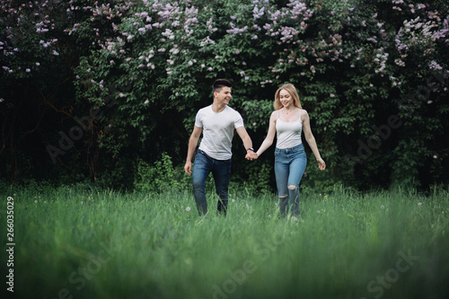 A young couple in love holding hands and walking forward in front of a flowering bush