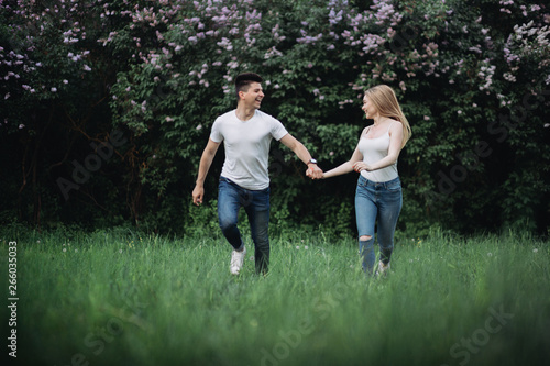 A young couple in love holding hands and running forward in front of a flowering bush