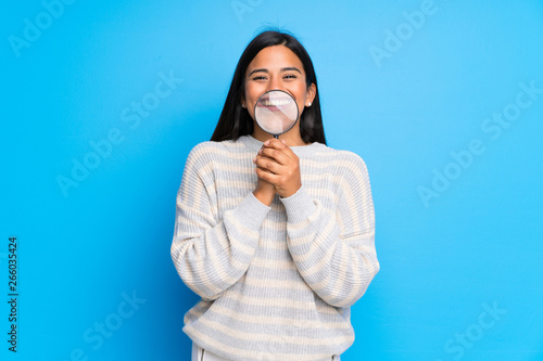 Young Colombian girl with sweater taking a magnifying glass and showing teeth through it