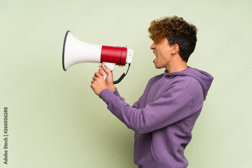 Young african american man over isolated green wall shouting through a megaphone Young african american man over isolated green wall shouting through a megaphone