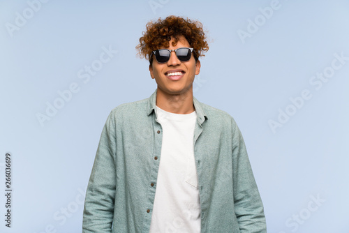 Young african american man over isolated blue wall with glasses and happy