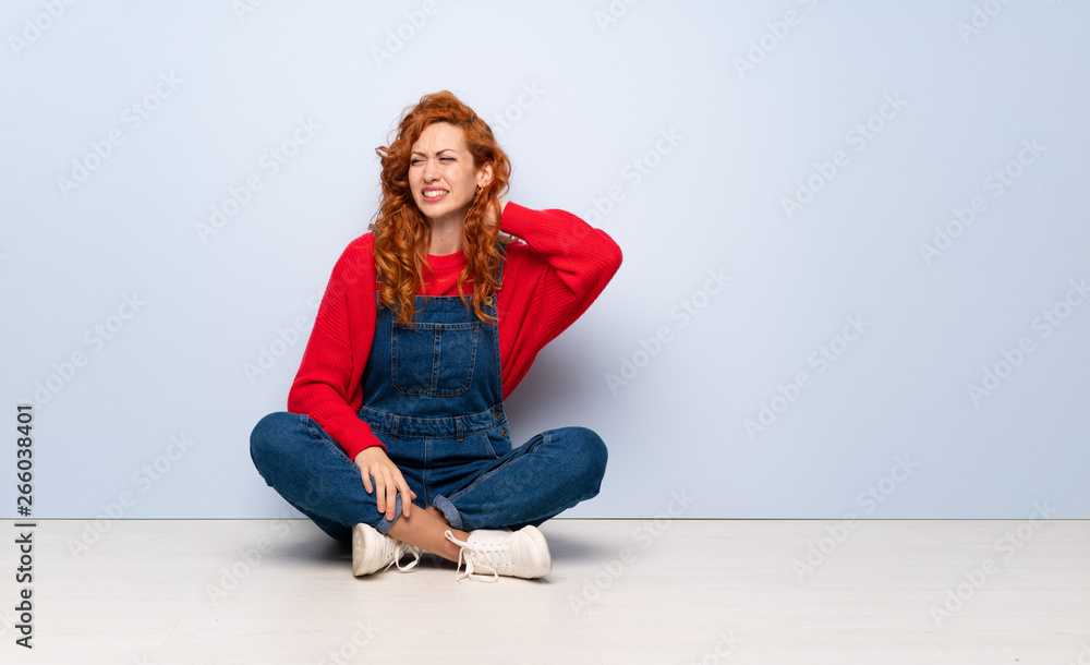 Redhead woman with overalls sitting on the floor with neckache Redhead woman with overalls sitting on the floor with neckache