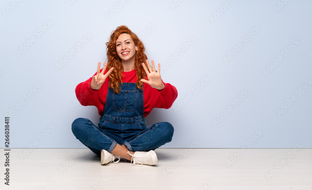 Redhead woman with overalls sitting on the floor counting eight with fingers Redhead woman with overalls sitting on the floor counting eight with fingers