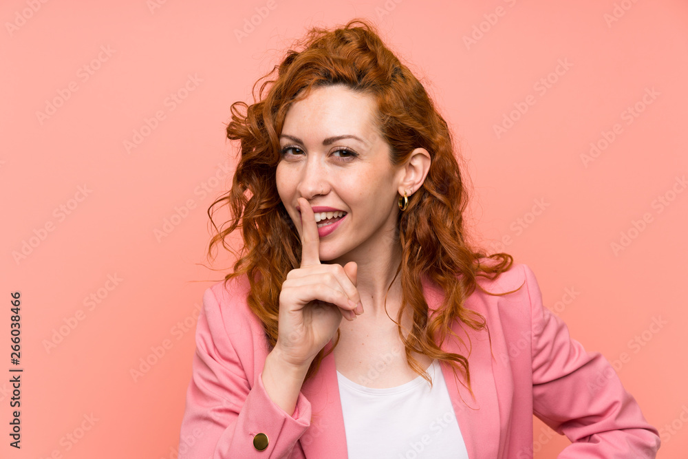 Redhead woman in suit over isolated pink wall doing silence gesture Redhead woman in suit over isolated pink wall doing silence gesture