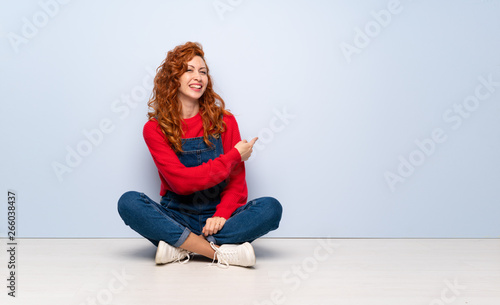 Redhead woman with overalls sitting on the floor pointing back