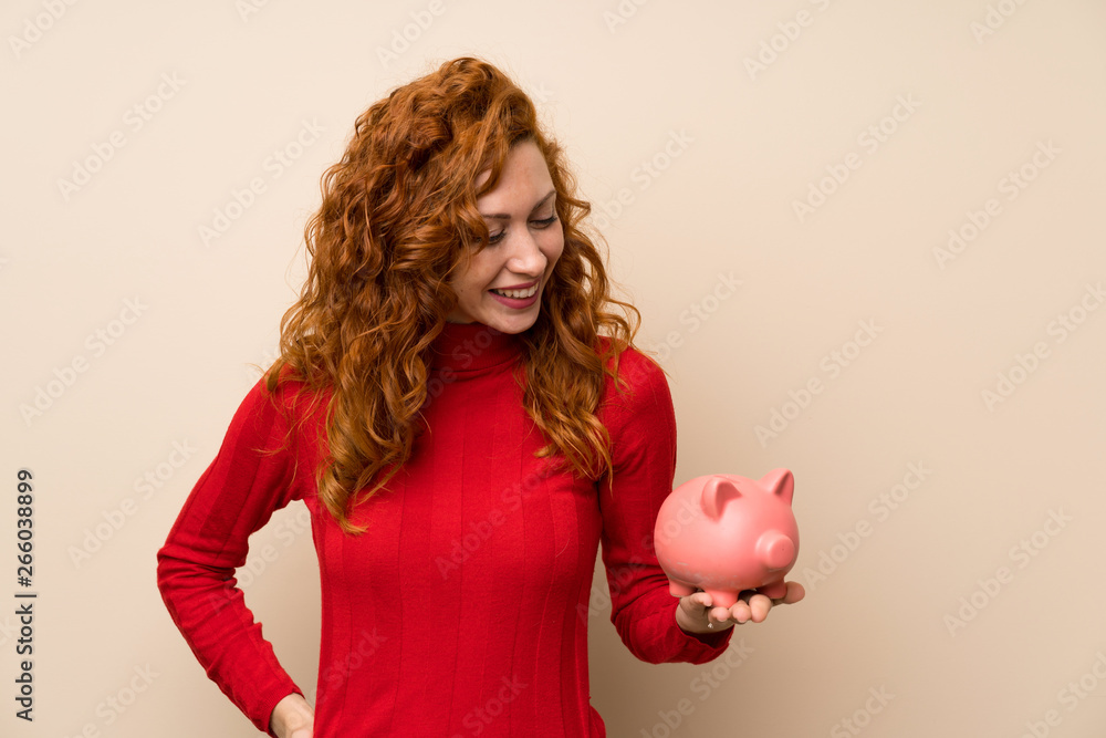 Redhead woman with turtleneck sweater holding a big piggybank Redhead woman with turtleneck sweater holding a big piggybank
