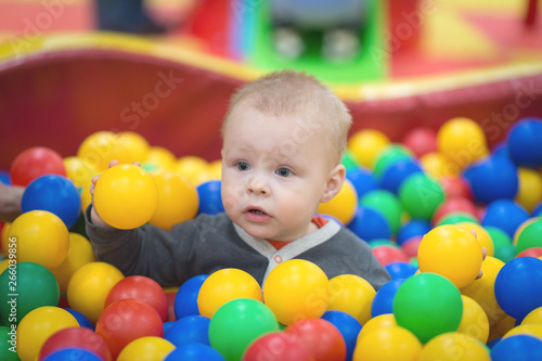 The boy sits in a pile of balls in a dry pool and plays