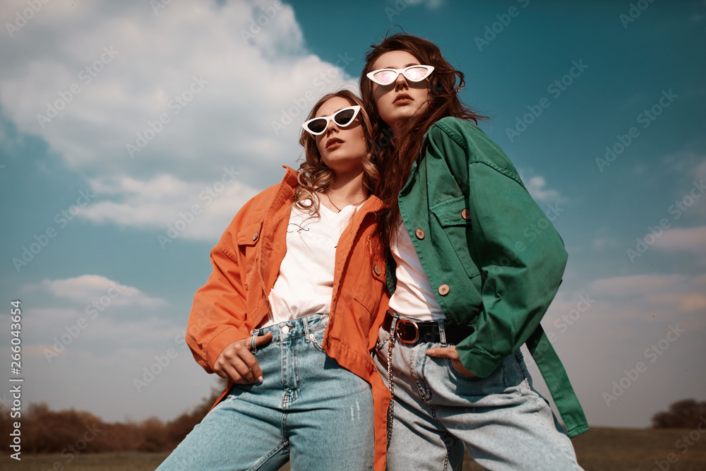 High fashion portrait of two stylish beautiful woman in trendy jackets and jeans posing outdoor. Vogue style. - obrazy, fototapety, plakaty 