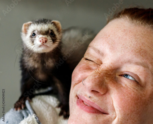 Schilderij op canvas Young attractive red head girl with freckles smiling at little ferret pet on her