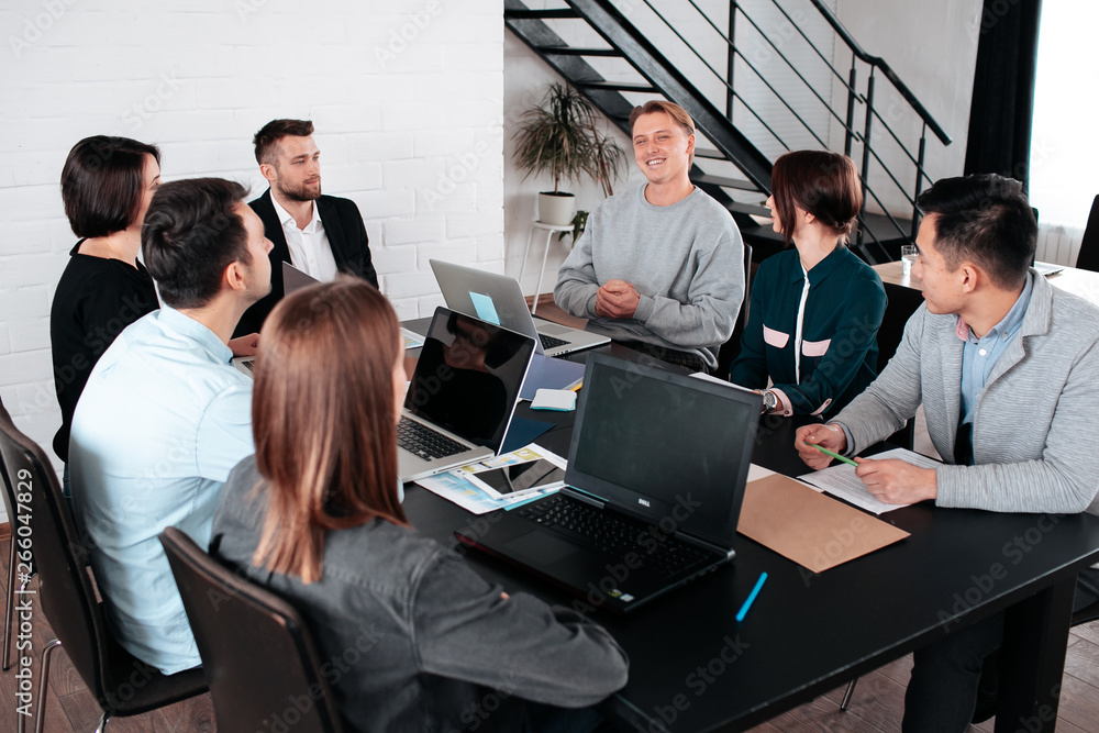 Making great decisions. Young beautiful man woman discussing something with smile while her coworkers listening to her sitting at the office table, group team young freelancers