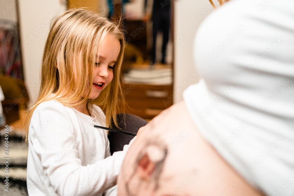 Obraz premium Little blonde girl painting little baby brother or sister on her mothers pregnant belly with water colors