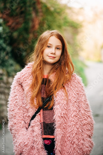 Outdoor close up portrait of pretty young red-haired girl wearing pink fluffy coat