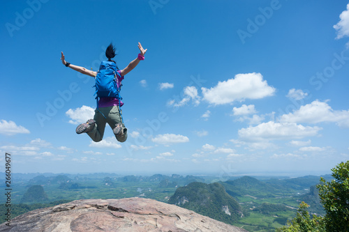 Happy successful woman hiker jumping on mountain peak cliff edge