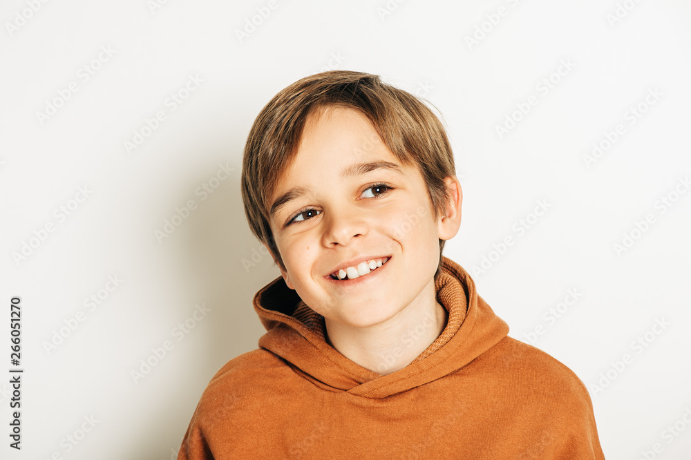Studio shot of handsome 10 year old boy with blond hair, wearing brown hoody, posing on white
