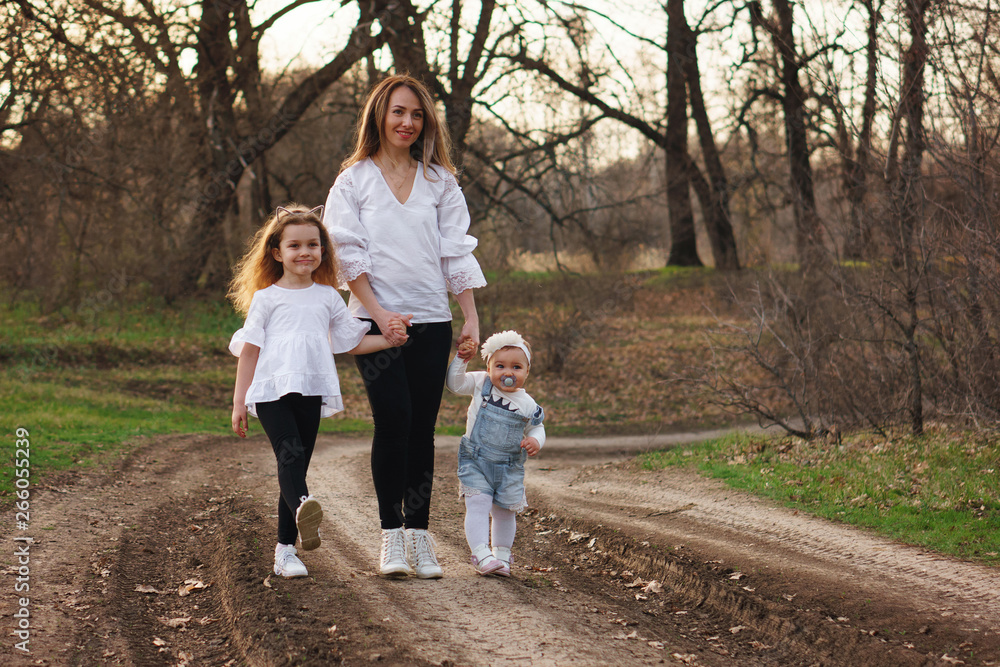 Happy family walking along path forest. Mother, oldest daughter and toddler, holding hands and gathering together. The concept of family ties. Spring mood Happy family walking along path forest. Mother, oldest daughter and toddler, holding hands and gathering together. The concept of family ties. Spring mood