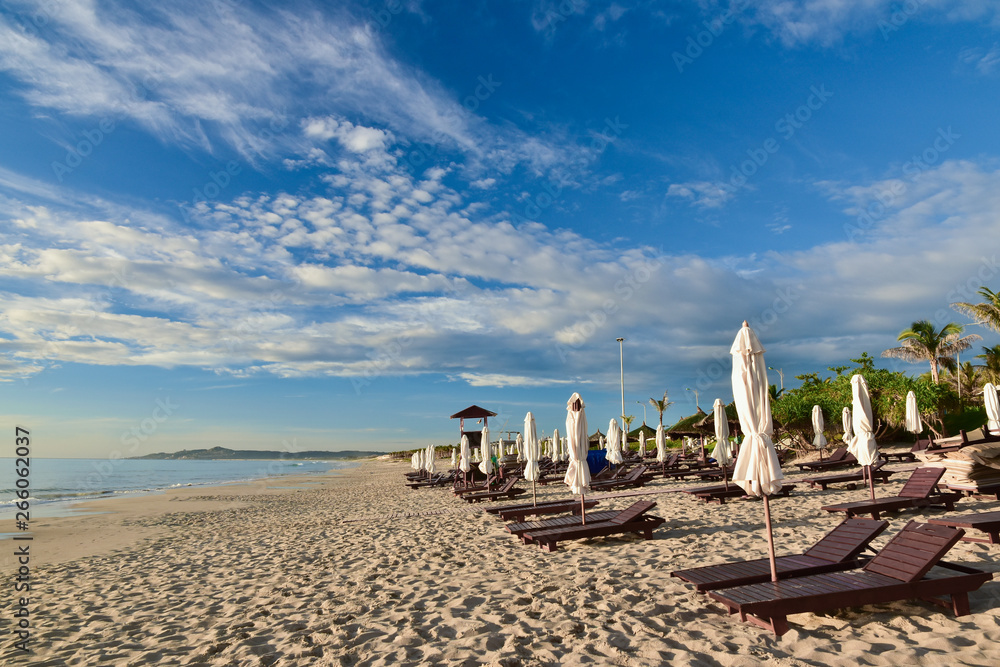 Sun loungers and umbrellas on an empty sandy beach. Summer sunny cloudy blue sky. Kamran. Vietnam. Copy space for text