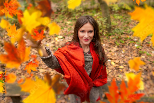Gorgeous young woman outdoors  in a park autumn scenery  throwing up in the air many yellow leaves  looking at the camera and smiling happy. Body shot  natural light  retouched  vibrant colors