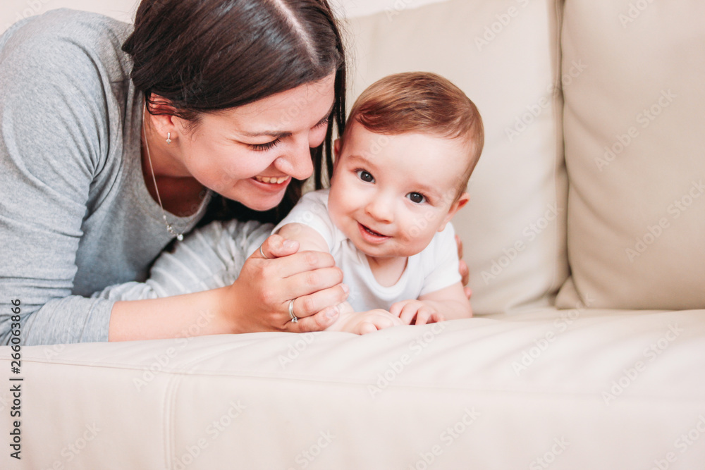 Charming little baby boy 6 months with happy mother on sofa at home, close up candid portrait Charming little baby boy 6 months with happy mother on sofa at home, close up candid portrait