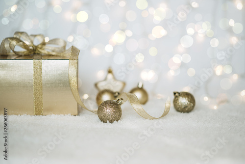 Christmas background with a gold decorations and gift box in snow on the blurred, sparkling background. Toned image with copy space. Selective focus.