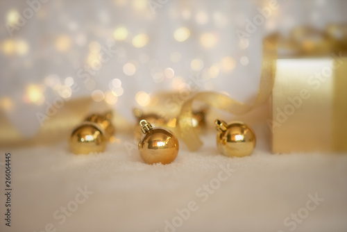 Gold Christmas background of defocused twinkling lights with gold balls, decoration and gift box. Selecnive focus. Toned image with copy space for your text.
