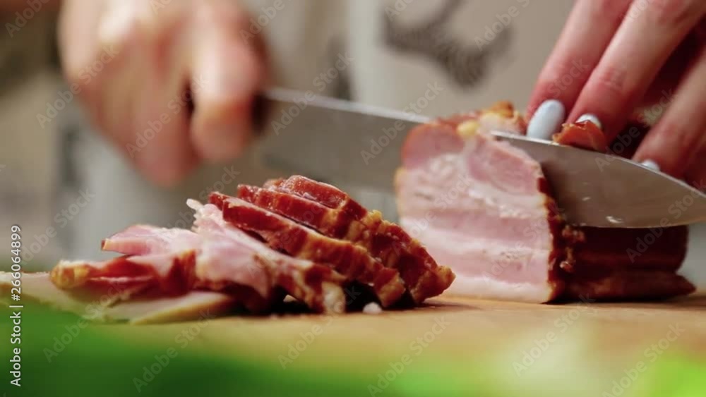Close-up of young female chef slicing delicious bacon on the cutting board in the kitchen Close-up of young female chef slicing delicious bacon on the cutting board in the kitchen