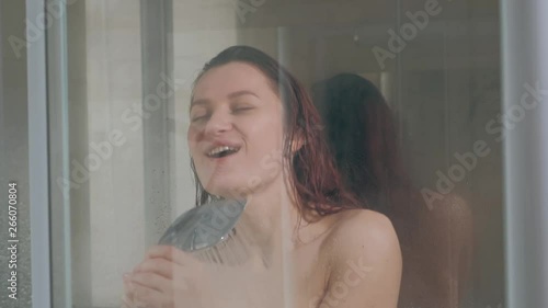Young beautiful woman in the shower. Glass cabin. Hot shower, steam and drops on the walls Sings in the watering can shower. Relaxation.