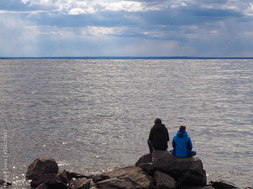 Two boys are sitting on the rocks looking on the sea