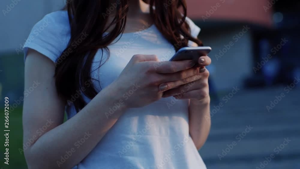 Close-up of young woman typing message on a smartphone while standing on the busy street of modern city. Close-up of young woman typing message on a smartphone while standing on the busy street of modern city.
