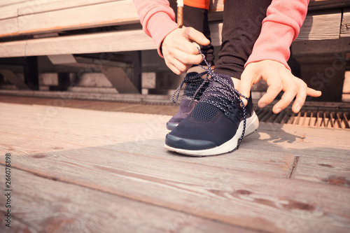 Close up of sporty woman tying shoelace while kneeling outdoor, In background bridge. Fitness outdoors concept