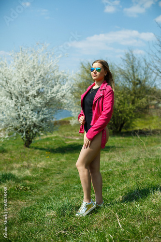 Girl in a black bodysuit and a pink jacket in nature with a flowering tree © Дмитрий Ткачук