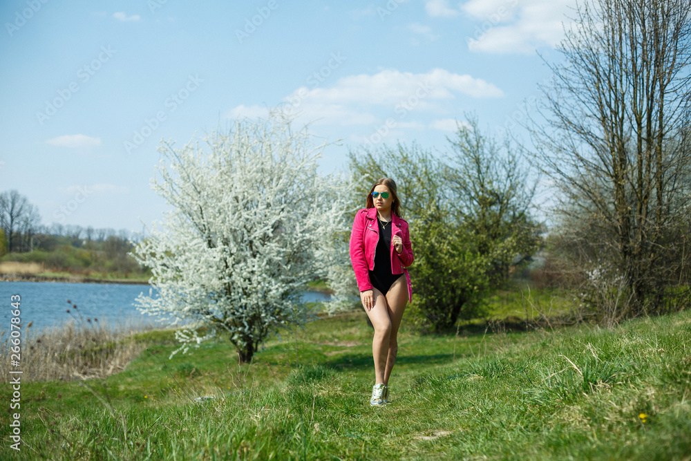 Girl in a black bodysuit and a pink jacket in nature with a flowering tree Girl in a black bodysuit and a pink jacket in nature with a flowering tree