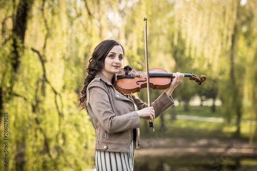 fashionable young woman thoughtfully and dreamily plays the violin in the park
