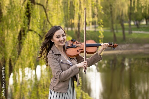 fashionable young woman emotionally playing the violin in the park