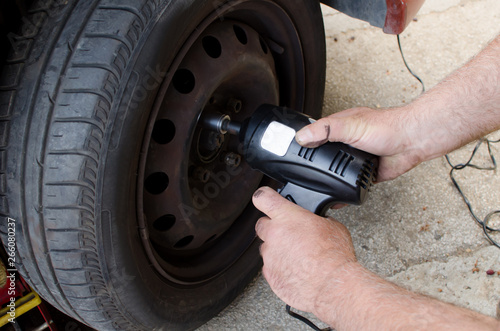 Mechanic changing wheel on car with impact wrench, man with electric screwdriver changing tire on street close up