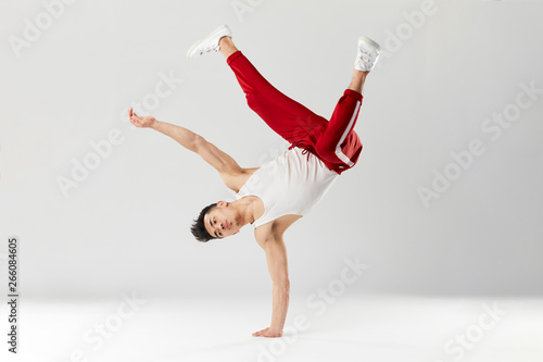 фотографія Athletic young b-boy standing on one hand while dancing break dance and doing downrock isolated over white studio background