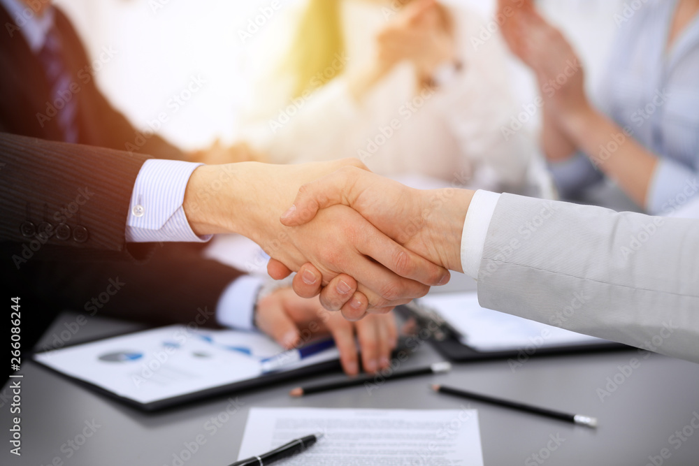 Business people shaking hands at meeting while theirs colleagues clapping and applauding. Group of unknown businessmen and women in modern white office. Success teamwork, partnership and handshake Business people shaking hands at meeting while theirs colleagues clapping and applauding. Group of unknown businessmen and women in modern white office. Success teamwork, partnership and handshake