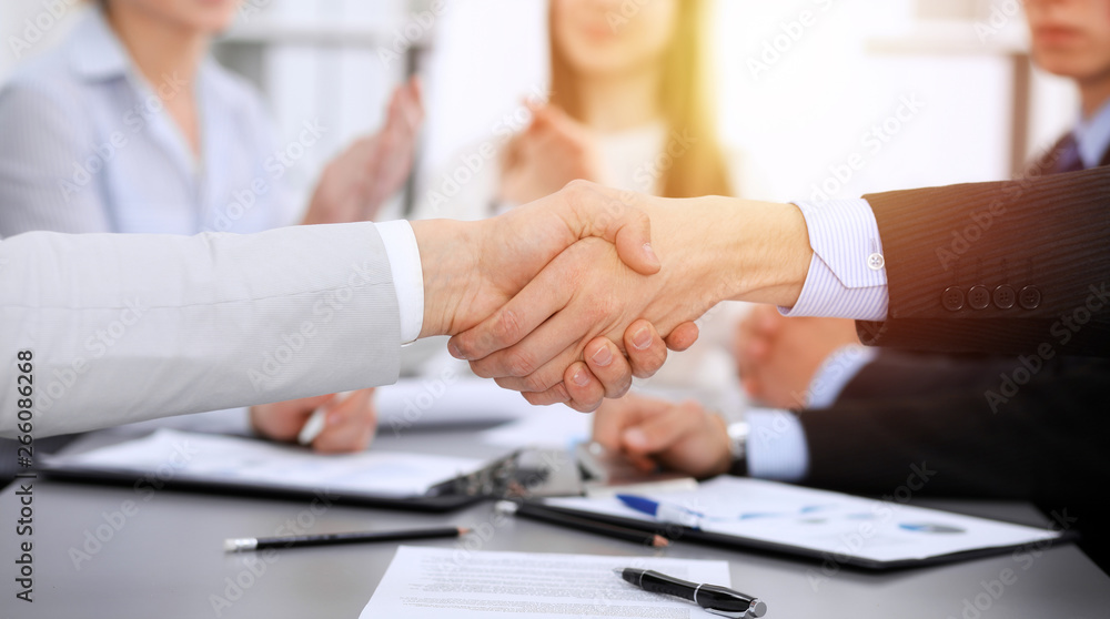 Business people shaking hands at meeting while theirs colleagues clapping and applauding. Group of unknown businessmen and women in modern white office. Success teamwork, partnership and handshake Business people shaking hands at meeting while theirs colleagues clapping and applauding. Group of unknown businessmen and women in modern white office. Success teamwork, partnership and handshake