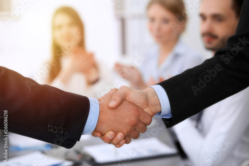 Business people shaking hands at meeting while theirs colleagues clapping and applauding. Group of unknown businessmen and women in modern white office. Success teamwork, partnership and handshake