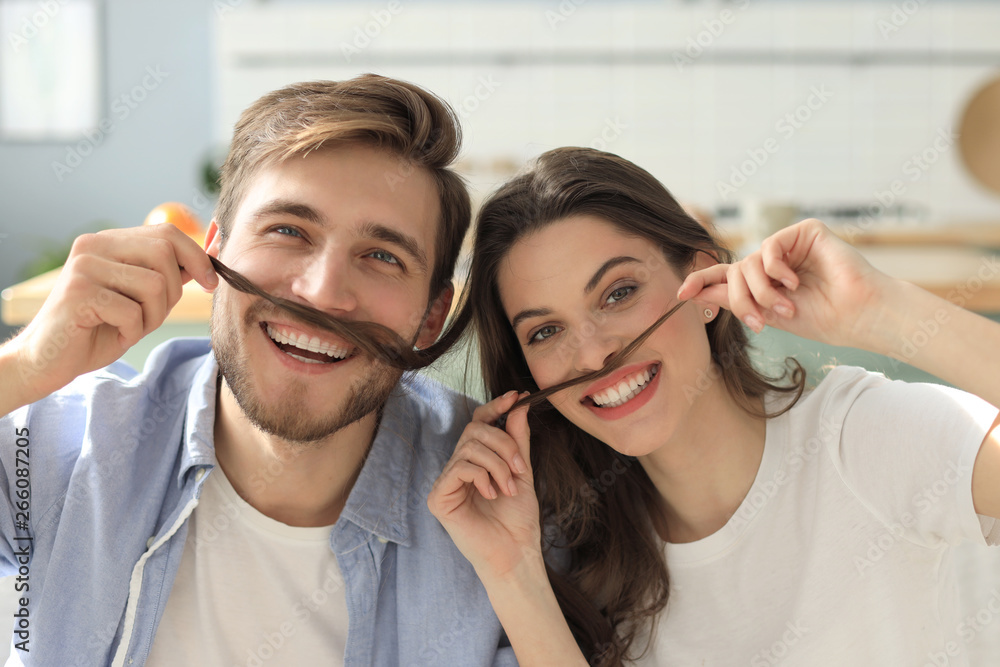 Portrait of cute young playful couple teasing with fake mustache sitting in sofa. Portrait of cute young playful couple teasing with fake mustache sitting in sofa.
