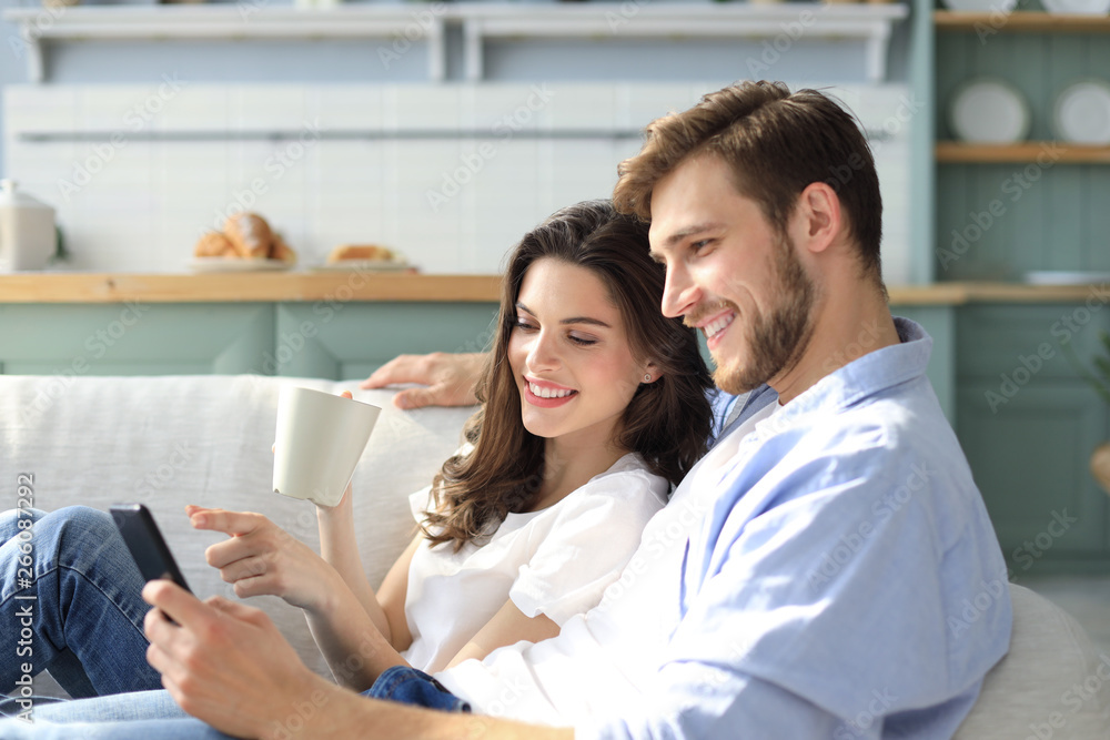 Young couple watching online content in a smart phone sitting on a sofa at home in the living room. Young couple watching online content in a smart phone sitting on a sofa at home in the living room.