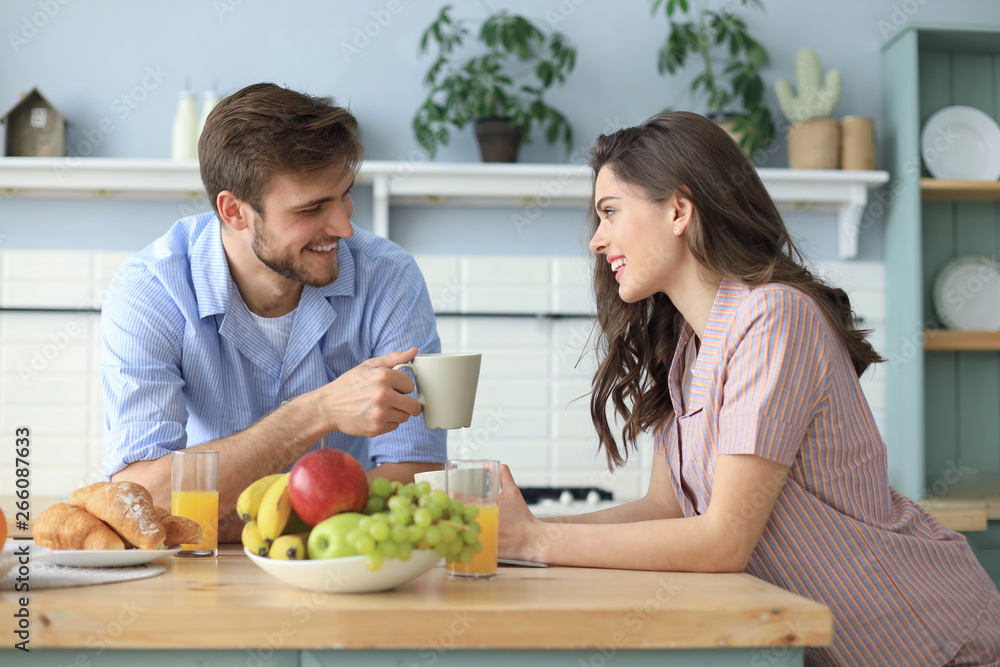 Beautiful young couple in pajamas is looking at each other and smiling while cooking in kitchen at home. Beautiful young couple in pajamas is looking at each other and smiling while cooking in kitchen at home.
