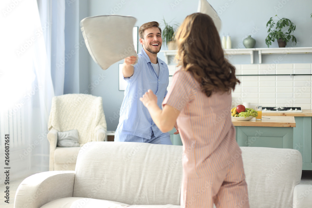 Obraz premium Happy loving couple having fun while having a pillow fight in the living room.