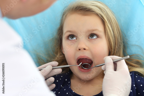 Little baby girl sitting at dental chair with open mouth and feeling fear during oral check up while doctor. Visiting dentist office. Medicine concept